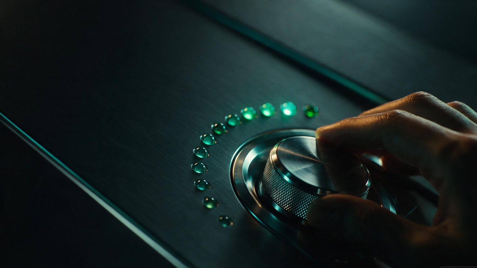 A hand turning a knurled metal control dial beside a rising arc of emerald indicator lights